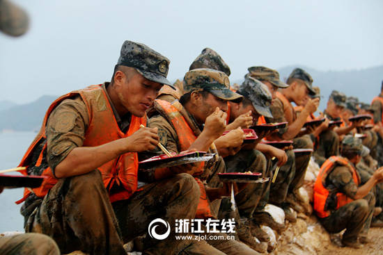 7月14日，九江赛湖大堤突降阵雨，为了节省时间，官兵们坐在大堤上就餐，吃完继续奋战。（朱万福摄）.jpg